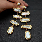 Gold and pearl drop earrings on a textured black surface