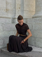 Woman in a black outfit sitting against a stone wall.
