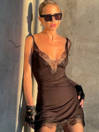 Woman wearing a brown lace dress and sunglasses against a concrete wall.