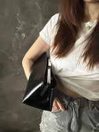 Person holding a black clutch bag against a dark background