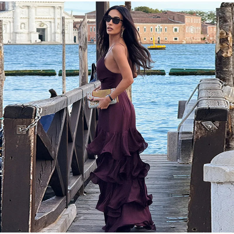 Woman in a purple dress standing on a wooden bridge over water with buildings in the background