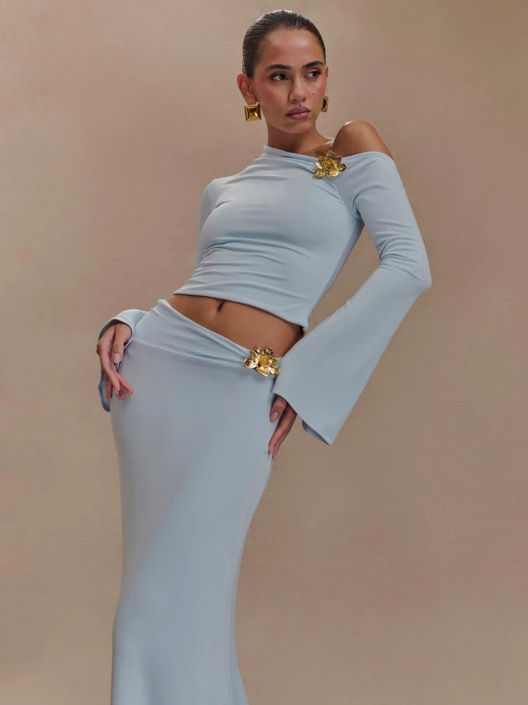 Woman wearing a light gray off-shoulder top and skirt with gold accents on a beige background