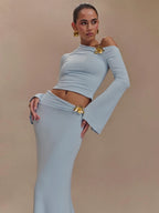 Woman wearing a light gray off-shoulder top and skirt with gold accents on a beige background