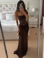 Woman in a brown evening gown taking a mirror selfie in a bedroom.