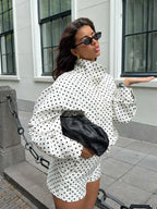 Woman in a polka dot outfit holding a black clutch against a building background