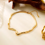 Gold bracelet on a light beige surface with a natural wood piece in the background