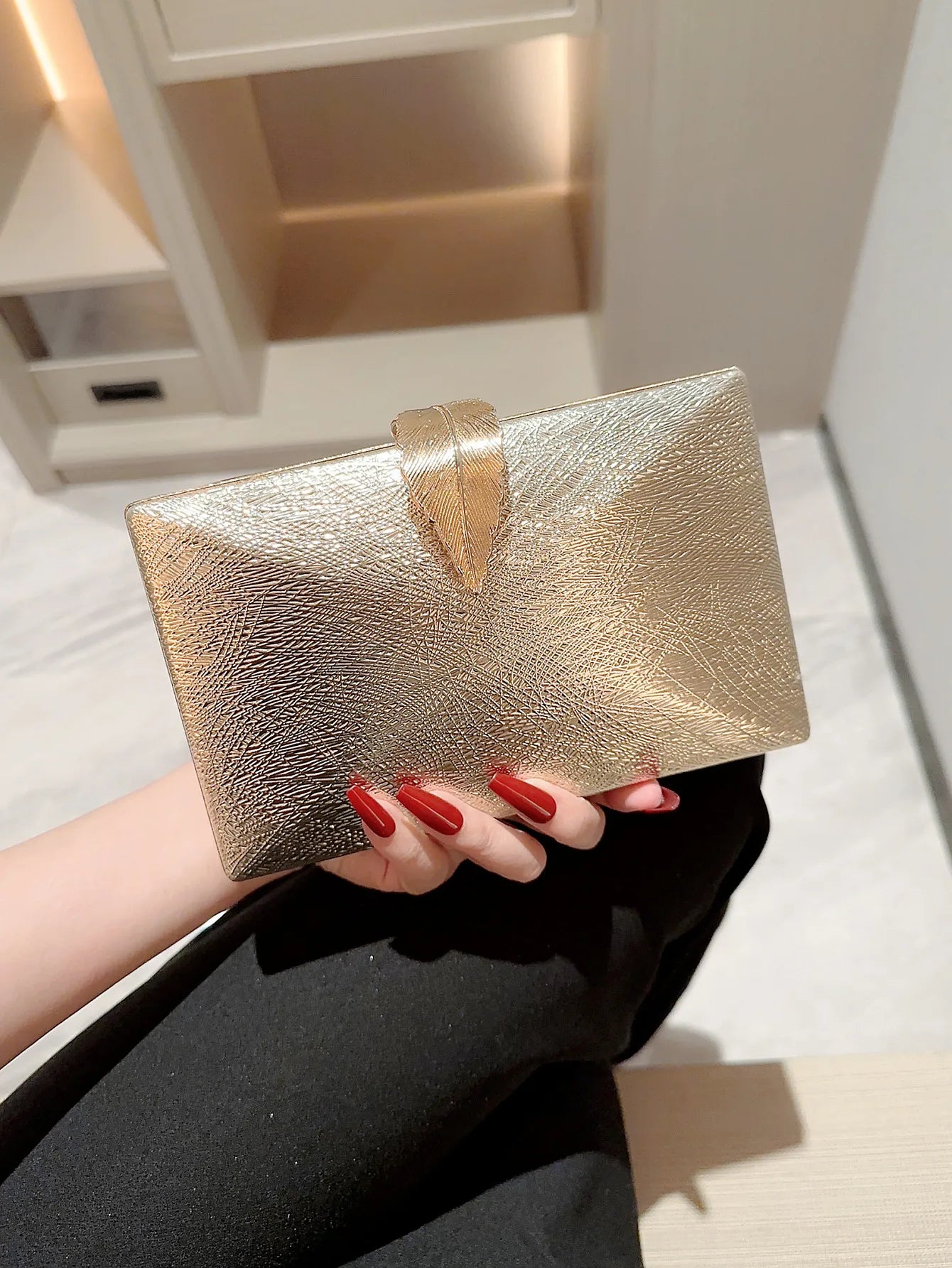 Gold clutch held by a hand with red nail polish on a light background