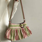 A pleated shoulder bag with vertical pink and sage green stripes, featuring a wide matching striped waistband and a dark brown circular metal ring detail, shown hanging against a light neutral background.