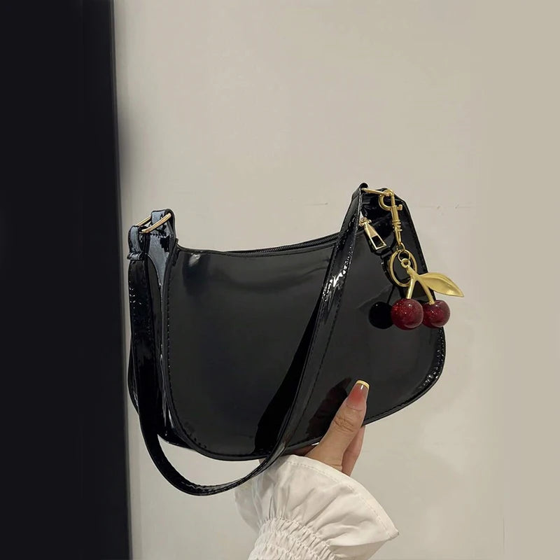 Black handbag with cherry charm held by a hand against a neutral background