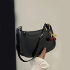 Black handbag with cherry charm held by a hand against a neutral background