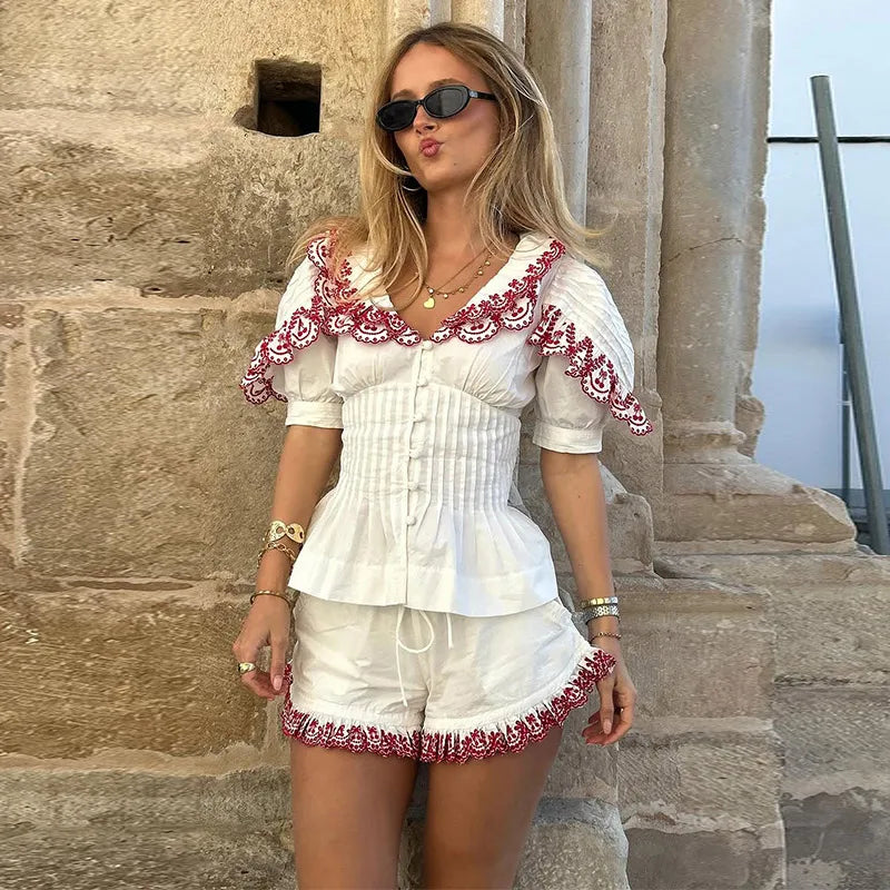 Woman in a white outfit with red details standing in front of stone architecture.
