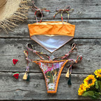 Orange bikini set with colorful straps on a wooden surface with sunflowers and a straw hat.