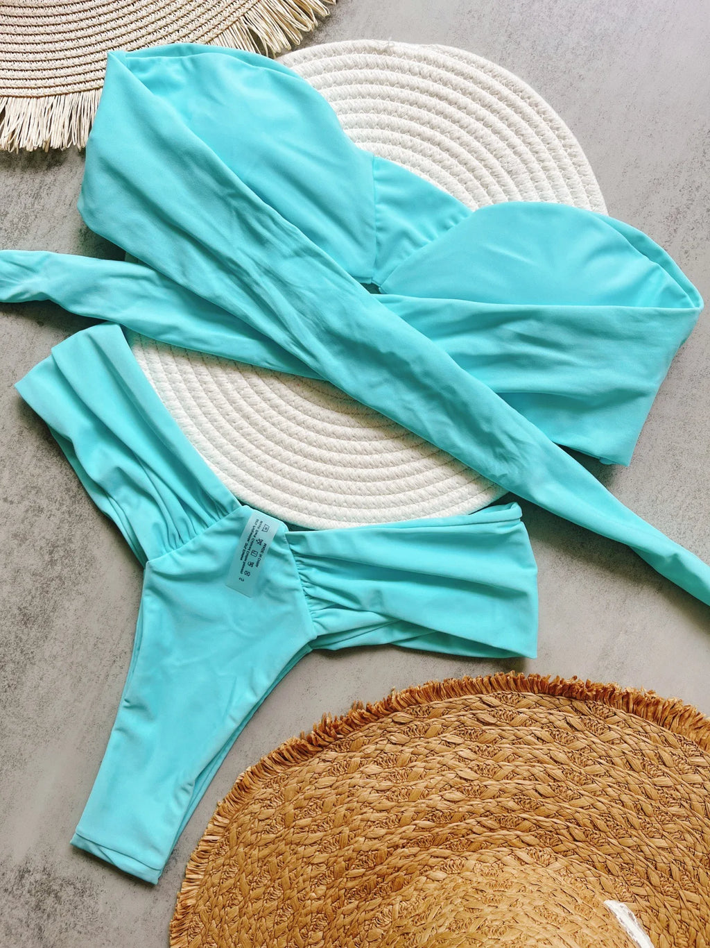Turquoise swimsuit laid out on a textured surface with a woven mat.