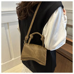 Person holding a brown suede handbag with a white shirt and black vest.