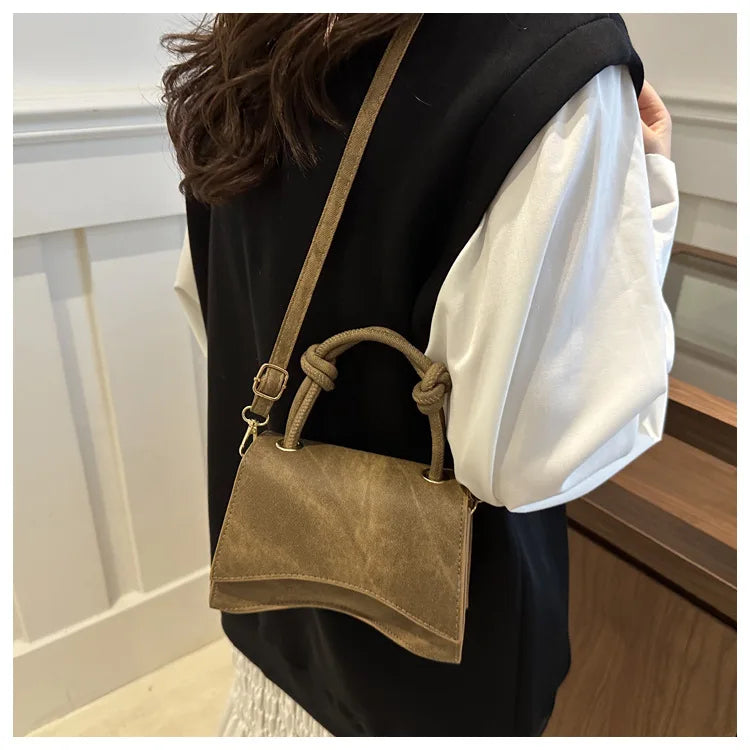 Person holding a brown suede handbag with a white shirt and black vest.