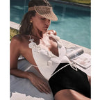 Woman in a white floral swimsuit and visor relaxing by a pool.