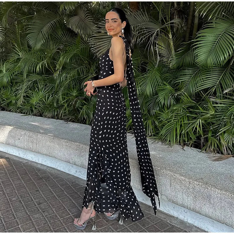 Woman in a black and white polka dot dress standing outdoors with greenery in the background