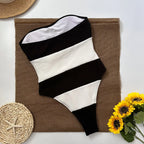 Black and white striped swimsuit on a brown mat with sunflowers and a woven hat.