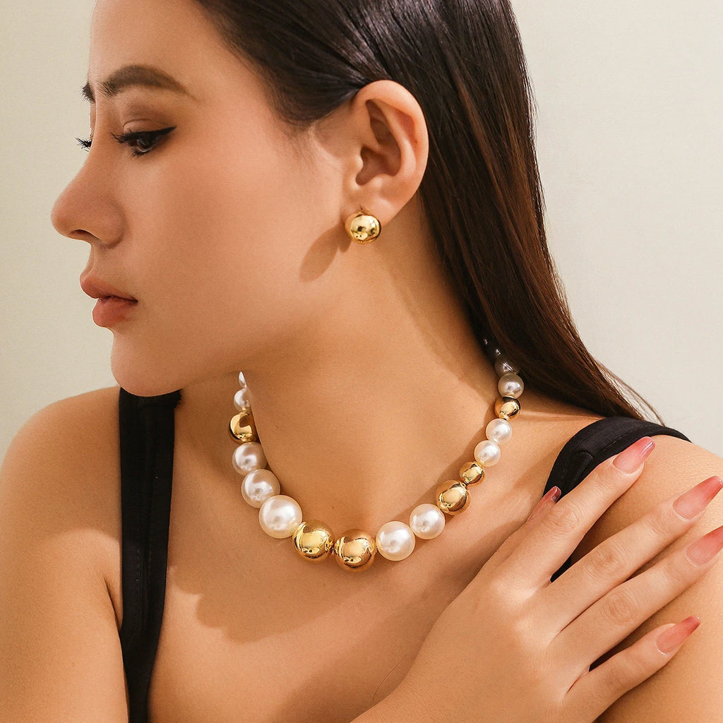Woman wearing a gold and pearl necklace with matching earrings against a neutral background
