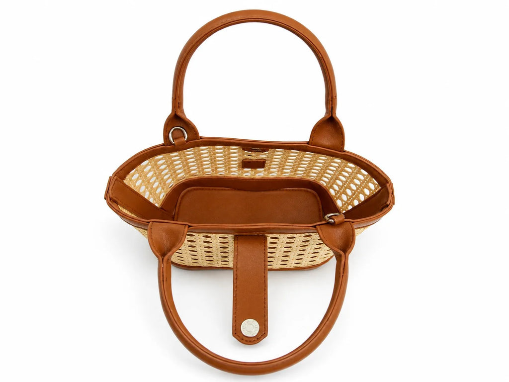 A structured handbag with a natural woven rattan body and warm brown leather trim, handles, and interior, shown from a top-down view on a white background.