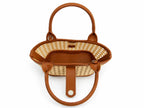 A structured handbag with a natural woven rattan body and warm brown leather trim, handles, and interior, shown from a top-down view on a white background.