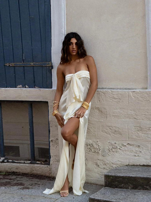 Woman in a strapless white dress with a high slit standing against a stone wall.