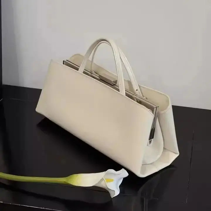 White handbag on a black surface with a white flower beside it