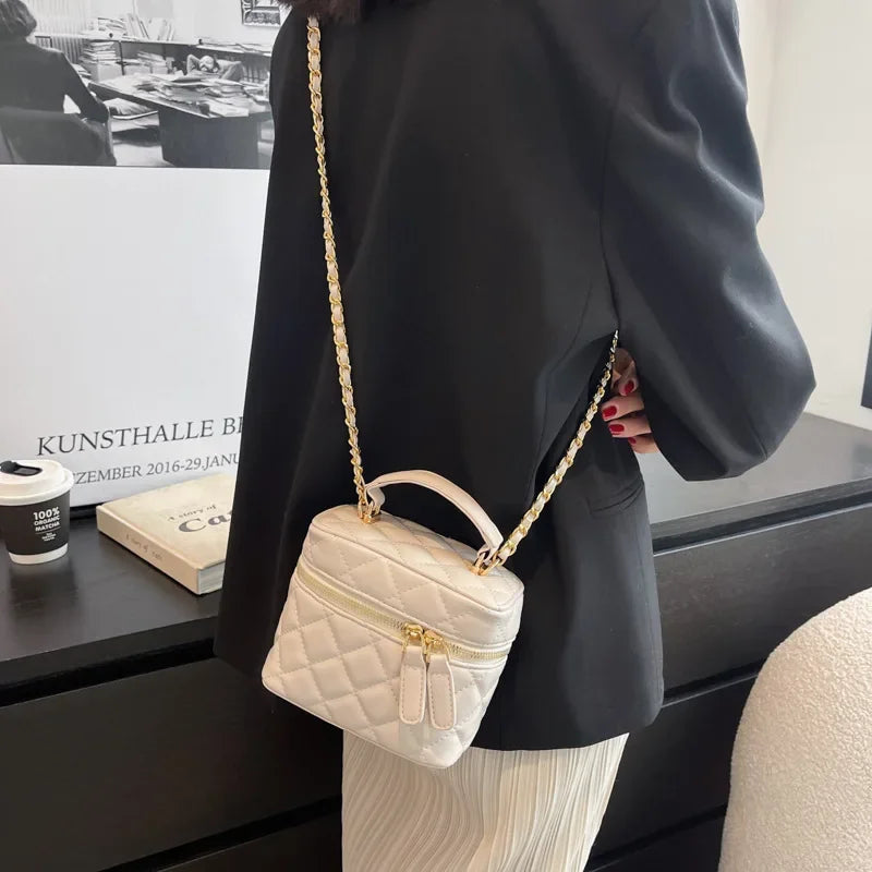 Person holding a beige quilted handbag with a gold chain strap in an indoor setting.