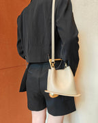 Person wearing a black outfit with a beige handbag against a textured wall.