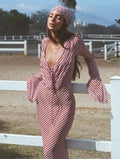 Woman wearing a red and white striped dress in an outdoor setting with a white fence and trees in the background.