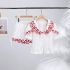 White blouse with red lace details on a hanger against a white background