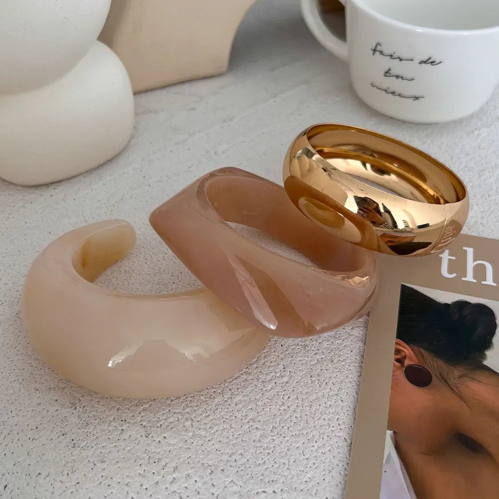 Gold and beige earrings on a textured surface with a blurred background