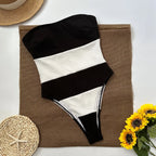 Black and white swimsuit on a brown fabric with sunflowers and a straw hat in the background