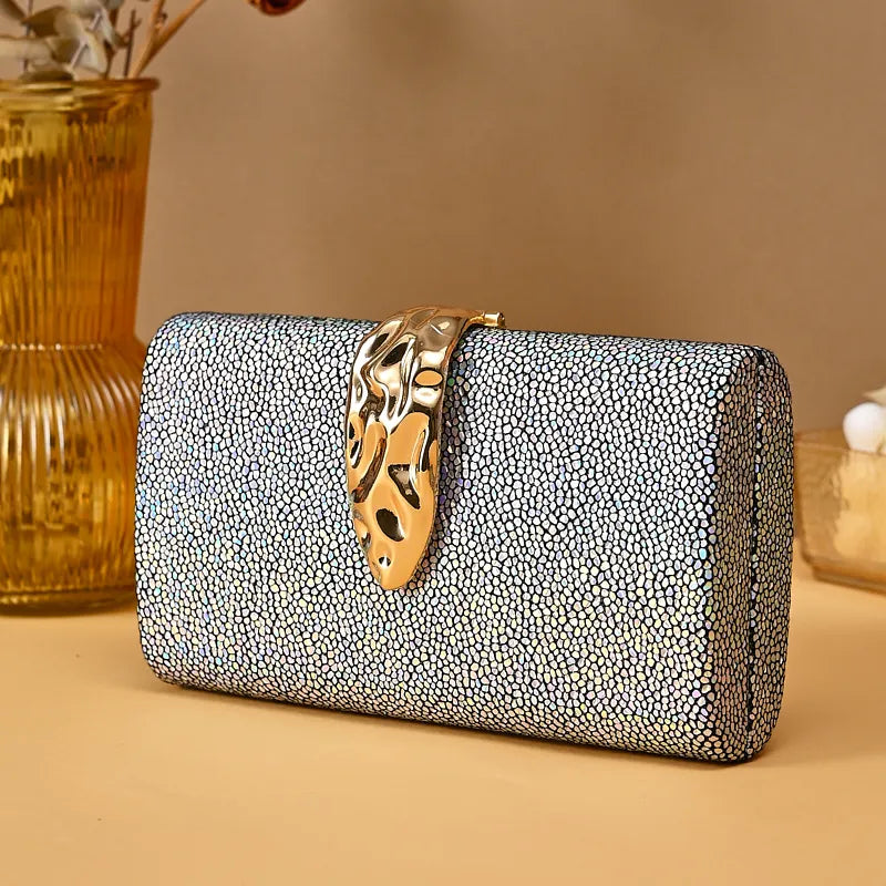 Silver textured clutch bag with a gold handle on a beige surface