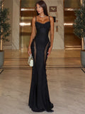 Woman in a black evening gown standing in an elegant interior setting.