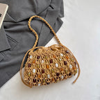 A woven straw handbag with a braided shoulder strap, decorated with colorful faux-amber and white stone accents, styled on a white surface next to a gray blazer.