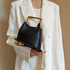 Person holding a black handbag with gold accents against a beige background