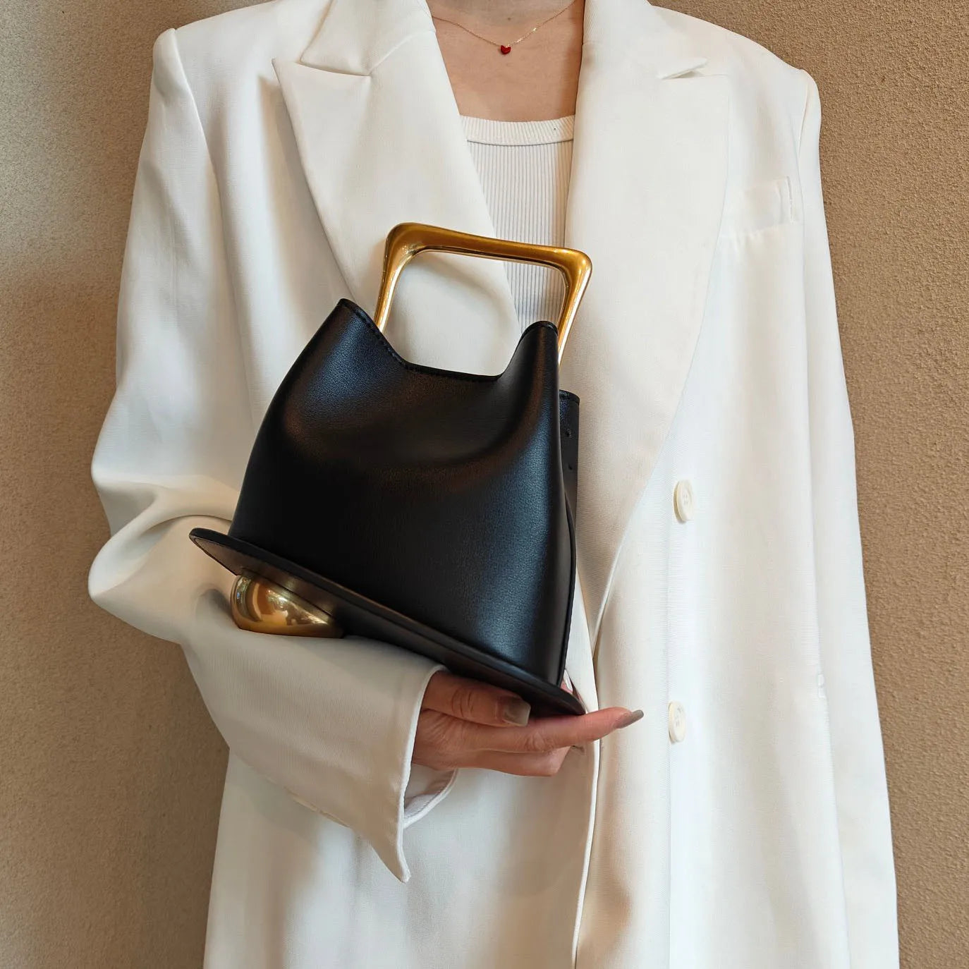 Person holding a black handbag with gold accents against a beige background
