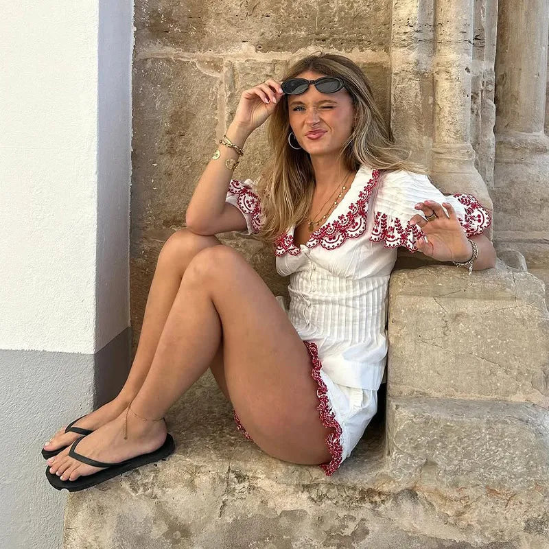 Woman in a white outfit with red embroidery sitting on stone steps.