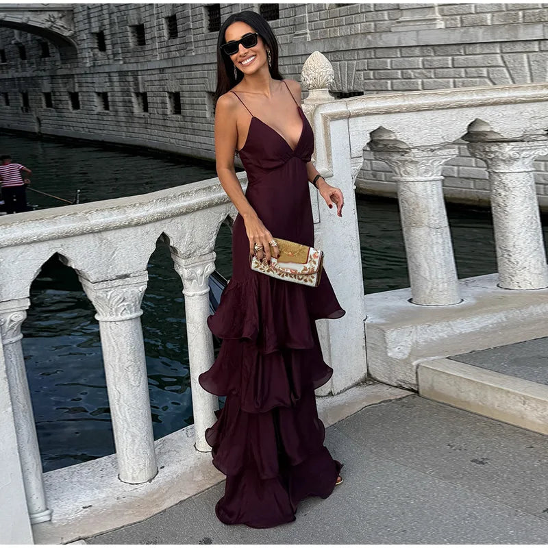 Woman in a deep purple dress standing on a stone bridge over water.