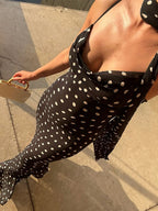Person wearing a black polka dot dress with a beige handbag on a concrete surface.