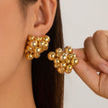 Gold sphere earrings being worn on an ear with a neutral background