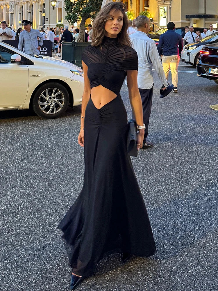 Woman in a black dress standing on a street with cars and people in the background