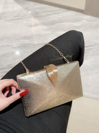Gold clutch bag held by a hand with red nail polish on a marble surface