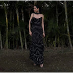 Woman in a black and white polka dot dress standing in a forest setting
