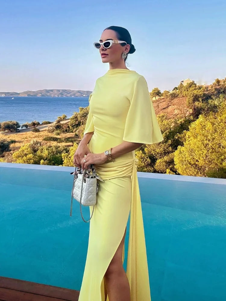 Woman in a yellow dress standing by a pool with a scenic background