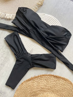 Black swimsuit top with a bow detail on a textured surface with woven mat