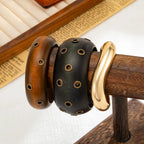 Three wooden bracelets with gold accents on a wooden stand.