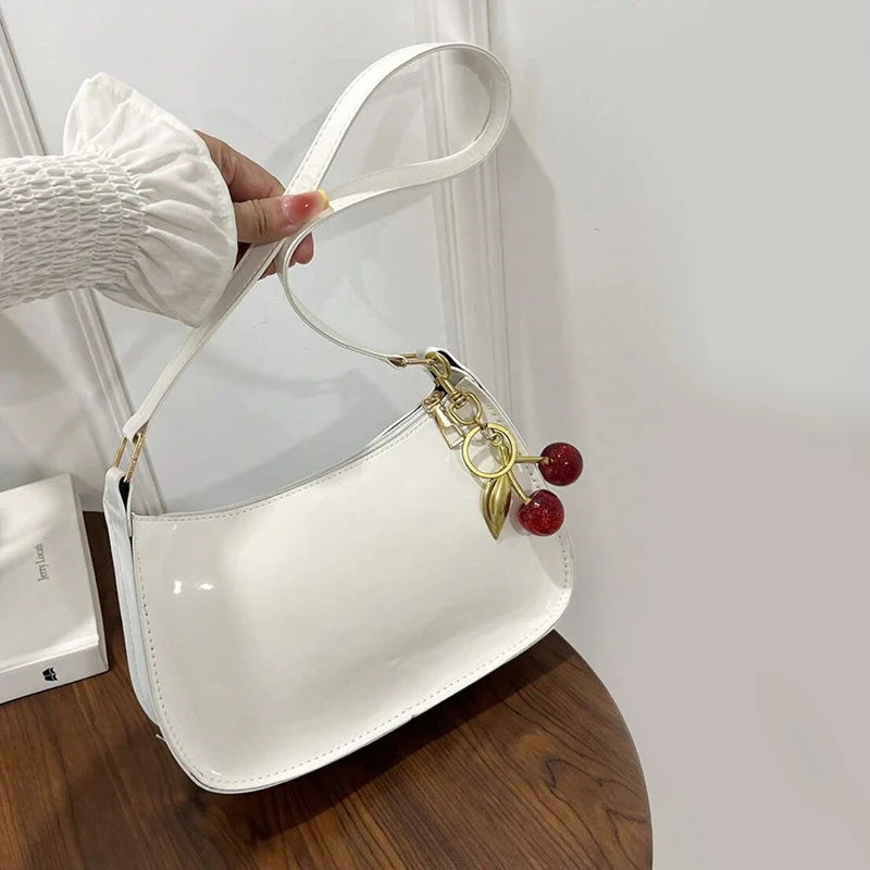 White handbag with decorative charm held by a person against a neutral background