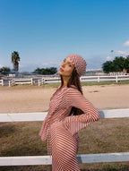 Woman in a red and white striped dress and headscarf standing outdoors with a clear blue sky.
